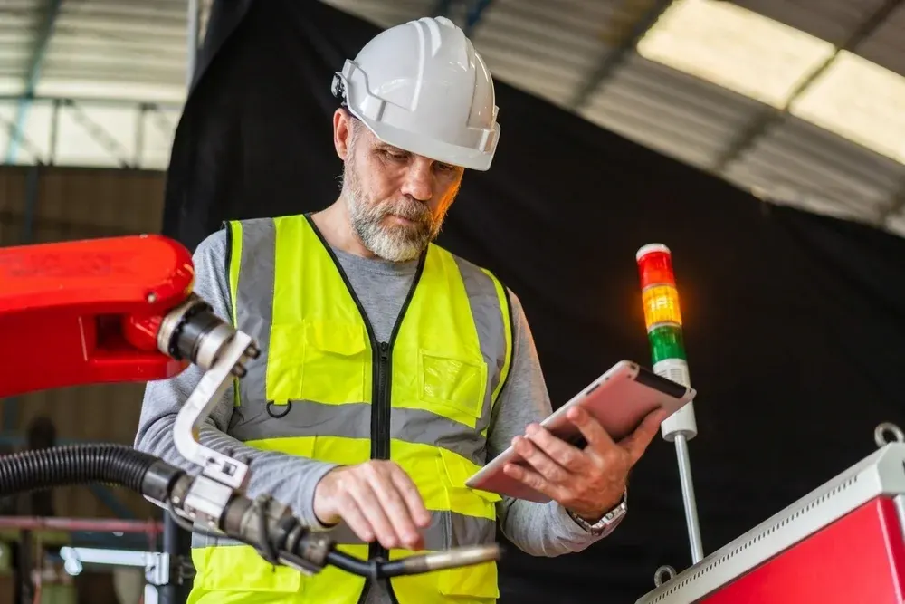 Factory operator checking machinery with a tablet beside an Andon signal light