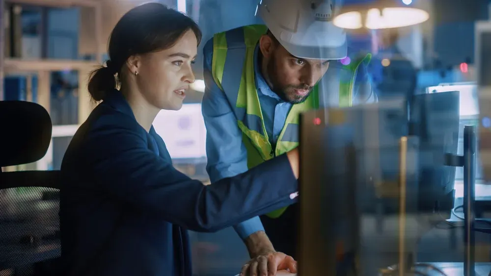Office team member and factory operator reviewing production information on a screen